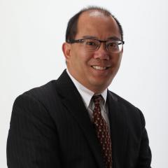 man with glasses in a black suit and red tie