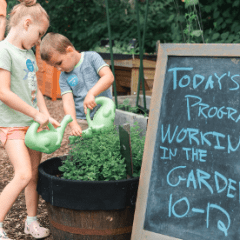 two children use small watering cans to water plants in a planter