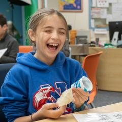a girl student smiles and laughs as she experiments with string and a paper cup to make a "laughing cup"