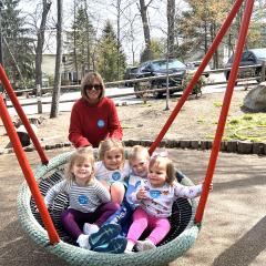 a grandmother pushes four young children in a large swing, outdoors