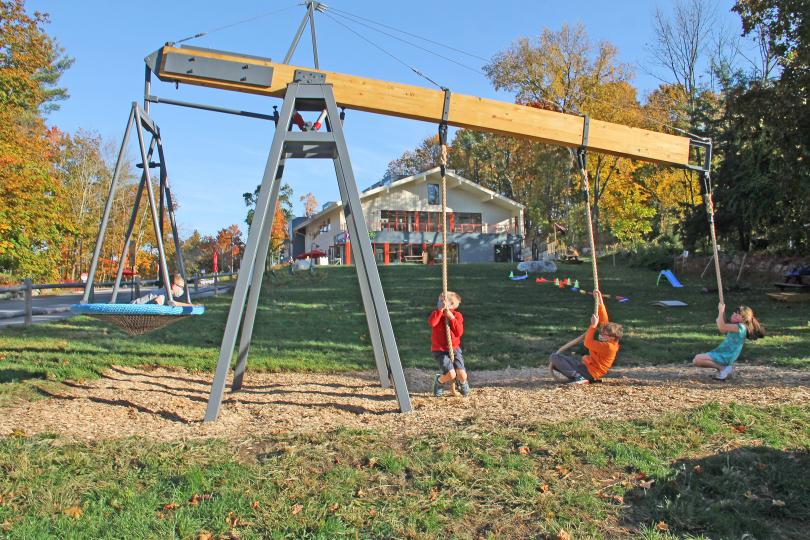 photo of a giant lever with a basket swing on one end, 3 pulley ropes on the other end, with kids in the basket and hanging on the ropes
