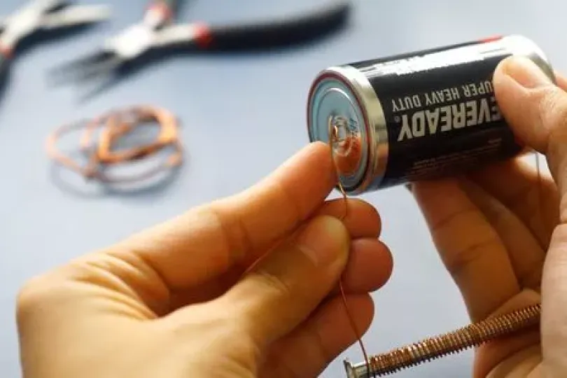 close up of hands holding a battery and pressing a wire to the positive end