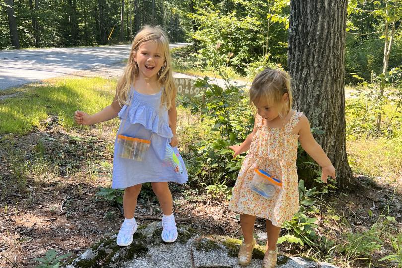 two young girls stand on a large rock