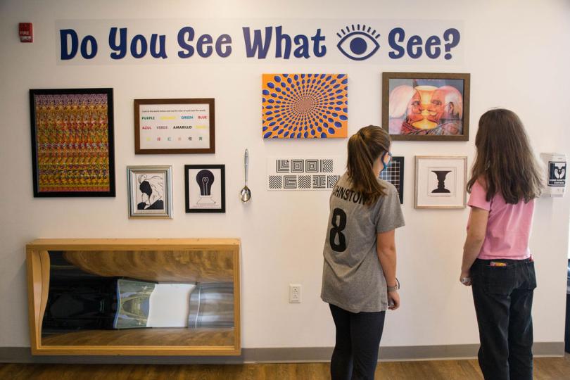 two teen girls look at an optical illusions exhibit together