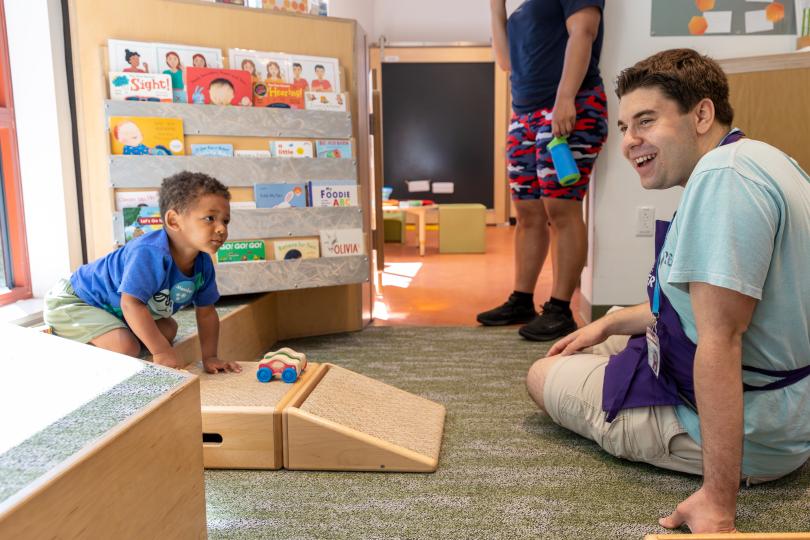 a young boy and a staff member play with cars on a ramp