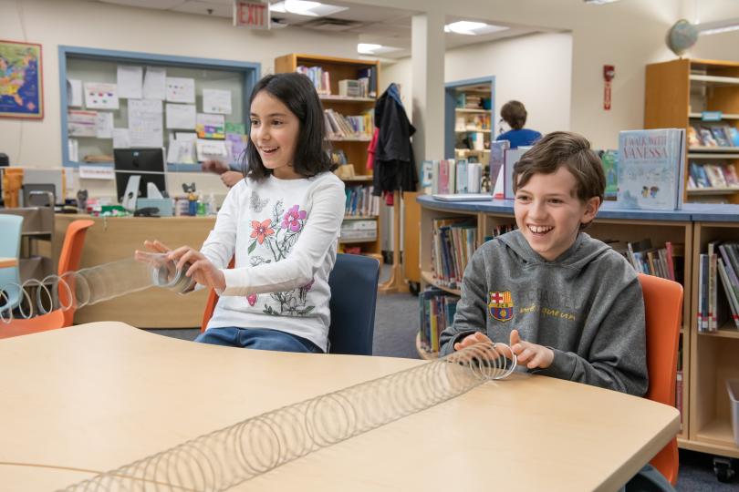 two middle-school students each hold the ends of an extended Slinky toy that is held by another student out of the frame