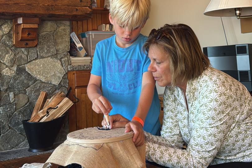 a grandmother works on a needlepoint project with her grandson