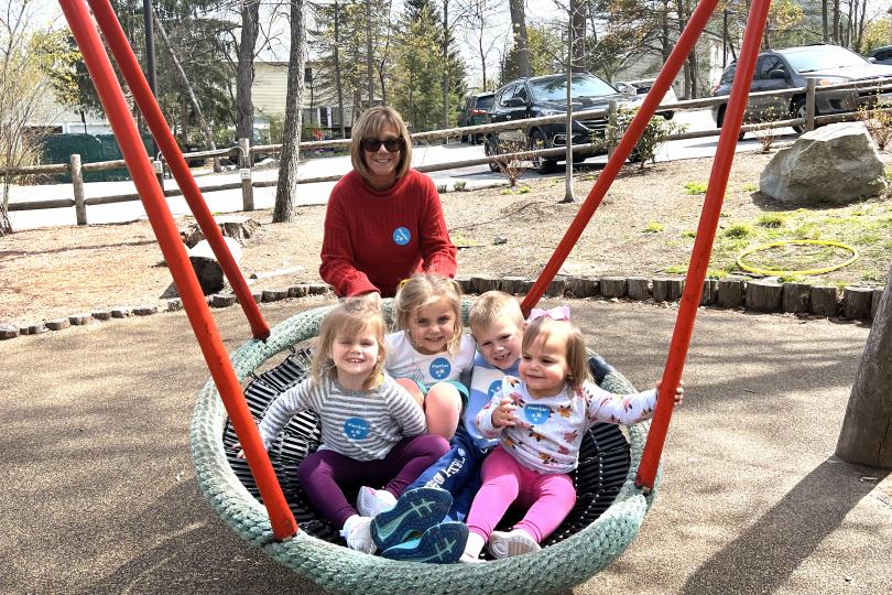 a grandmother pushes four young children in a large swing, outdoors