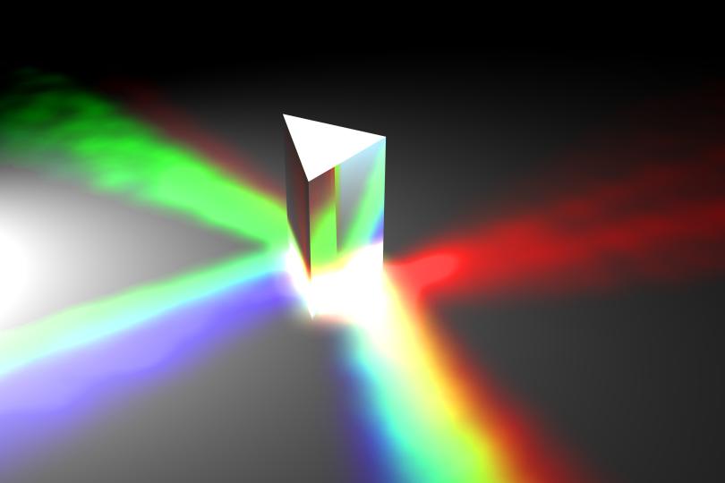 a prism sits on a table with different portions of the light spectrum emanating from different sides of the prism
