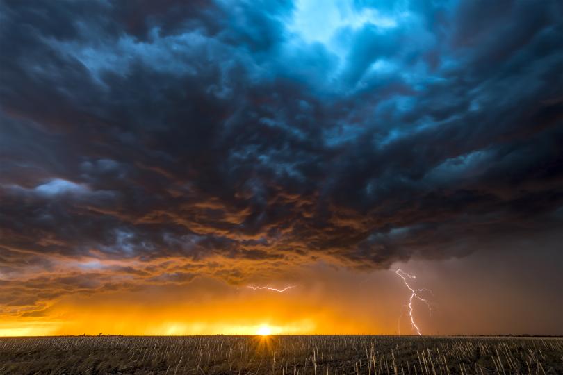 a sunrise or sunset on a dark horizon with dense dark clouds and a strike of lightning