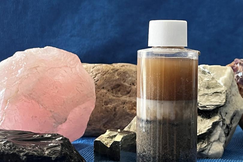 a closeup picture of rocks and minerals and a clear bottle with water and layers of sand, dirt, and sediment visible