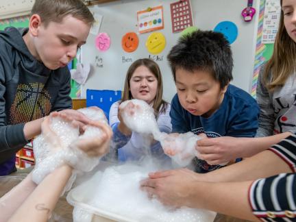 students crowd around a table with a foamy tub in the middle