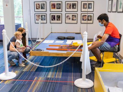 a mom and son watch as their harmonograph drawing is made, with a staff member