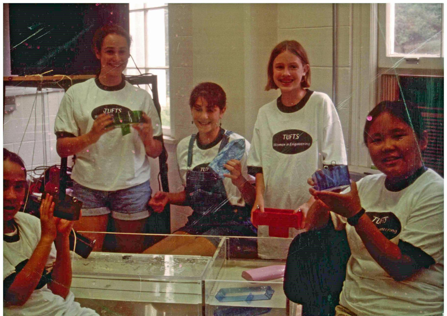 5 teenage girls in matching tshirts display a science exhibit they created; circa 1990