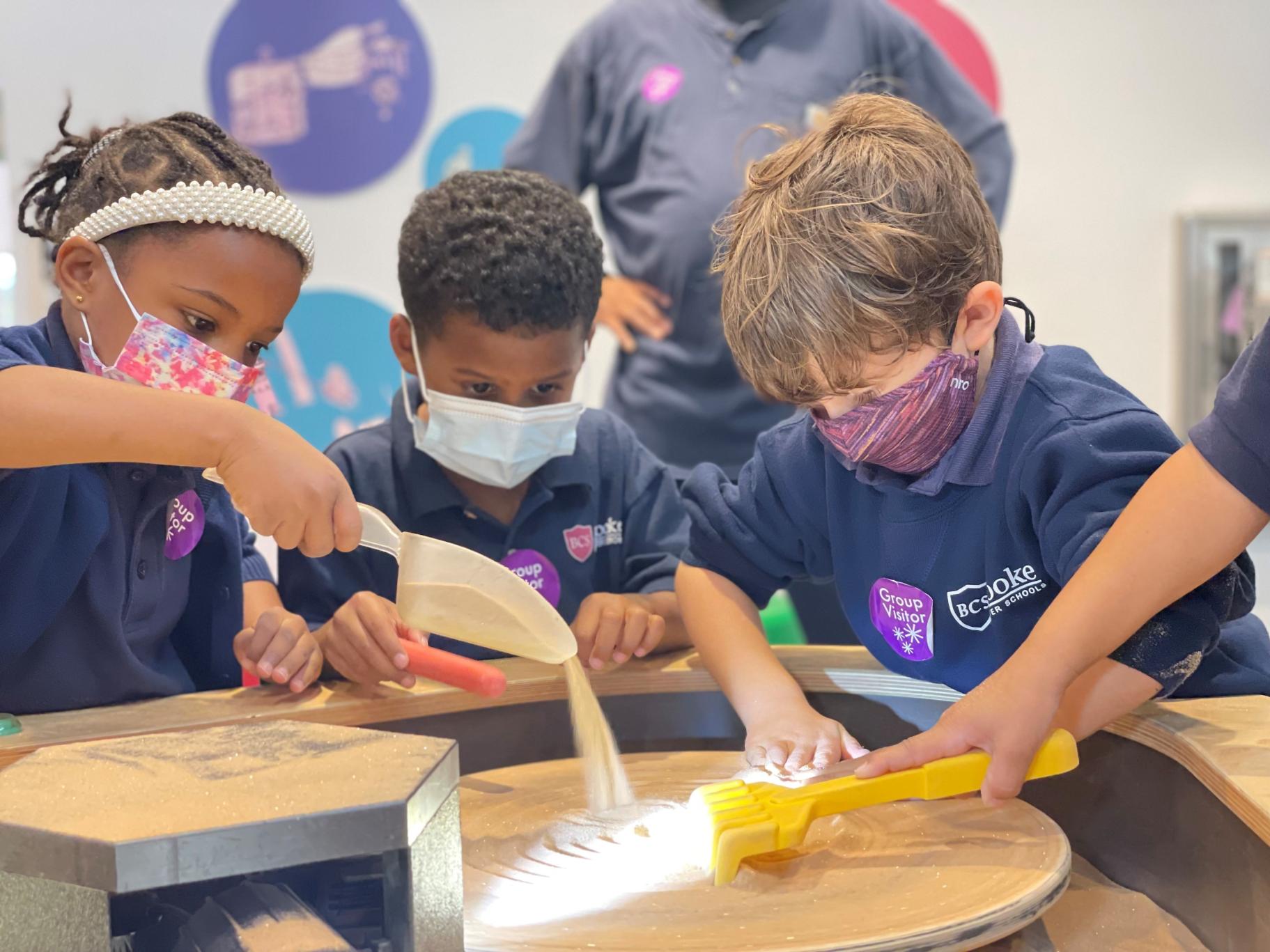 three children explore a sand exhibit