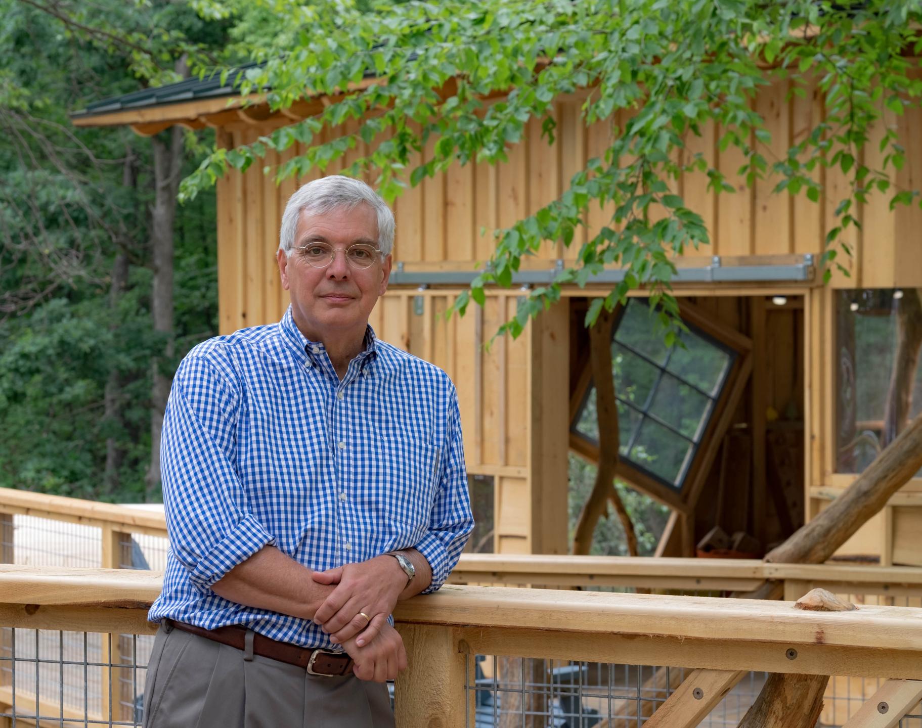 a man leans on a railing outside of a treehouse