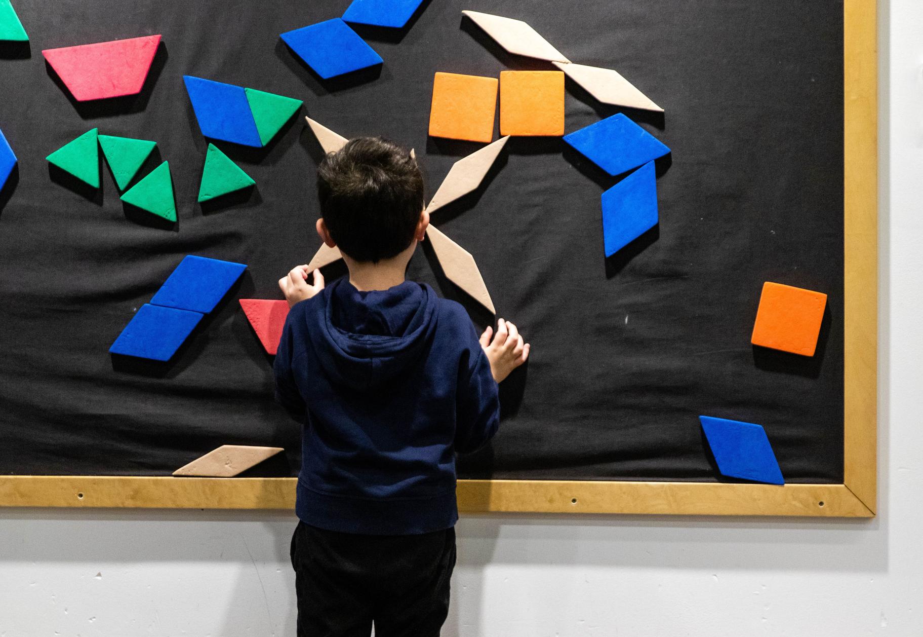 a boy stands and plays at a board of moveable geometric shapes