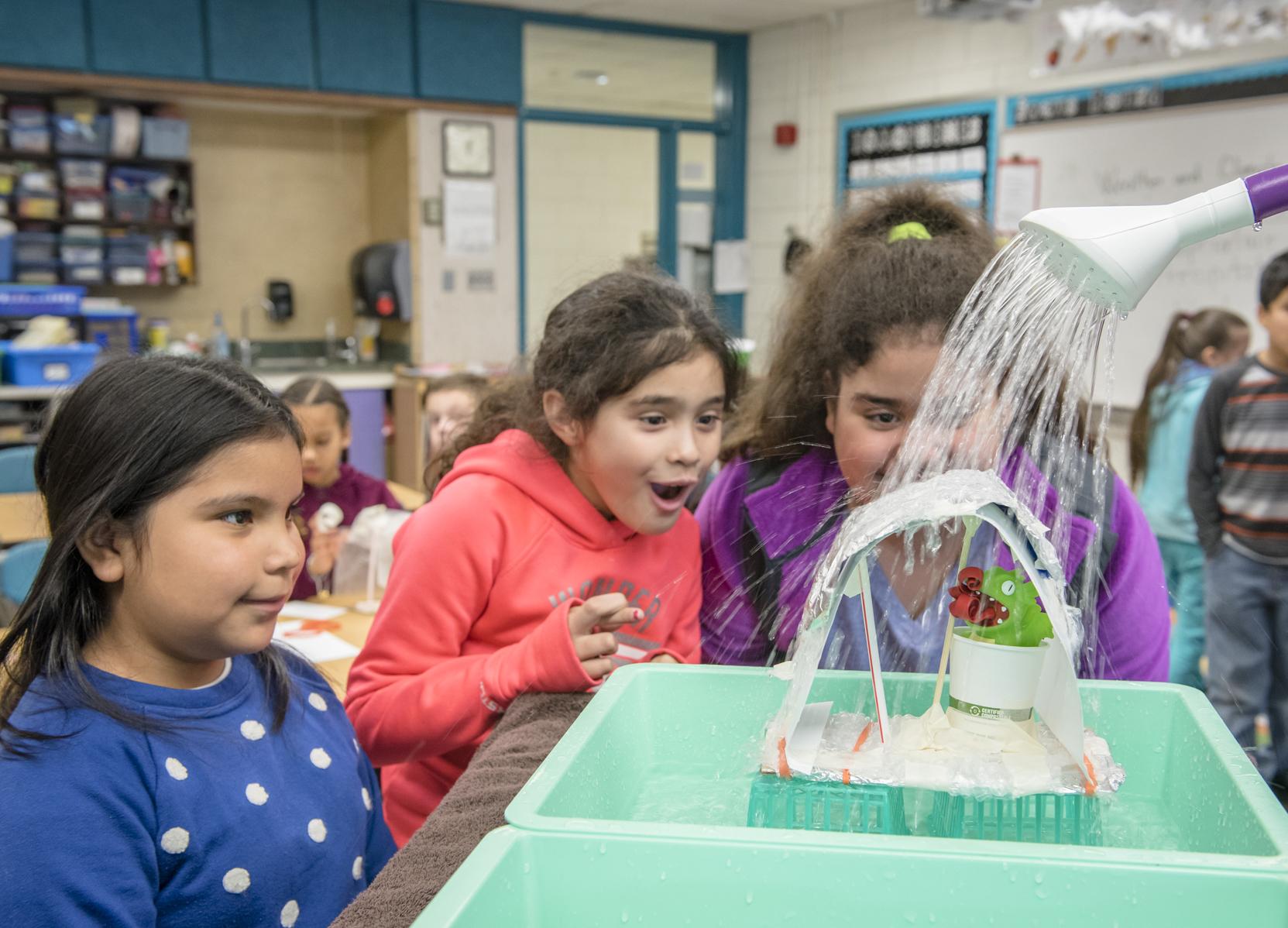 three 5th grade students watch the testing of their creation in a science workshop