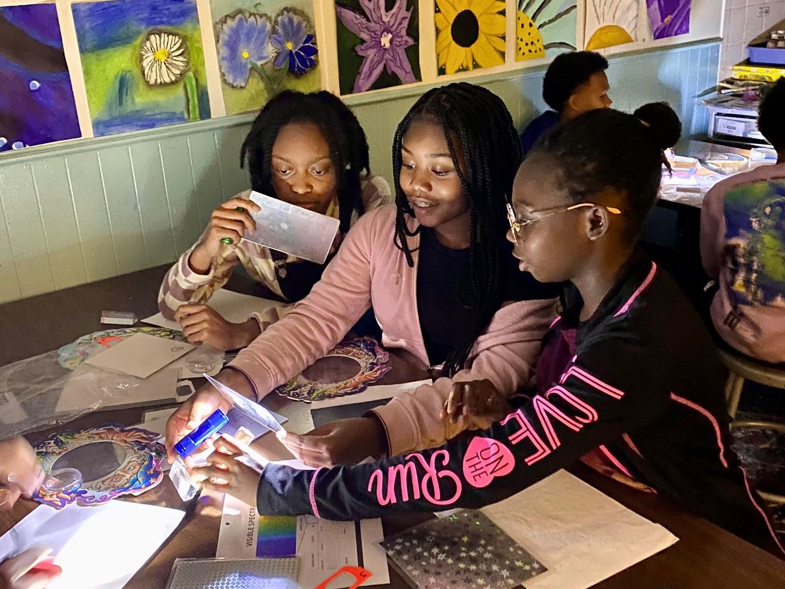 three students explore light and color in a darkened classroom