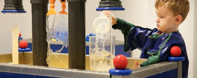 a young boy pours water from one container to another